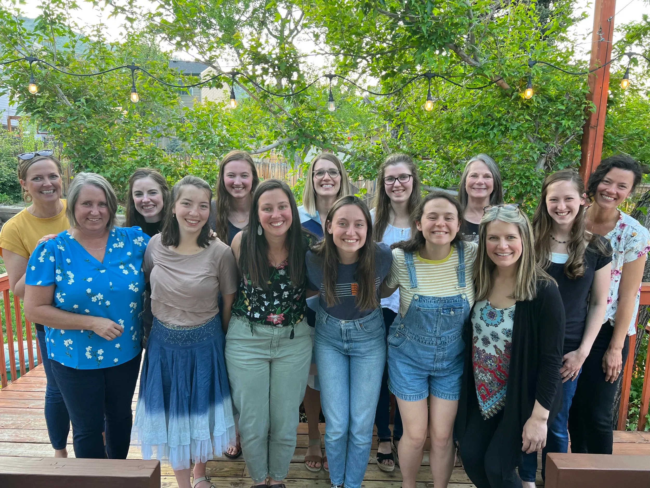 Women of Redeeming Grace Church gathered on a back porch under string lights